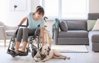Woman in wheelchair petting her dog laying on living room floor